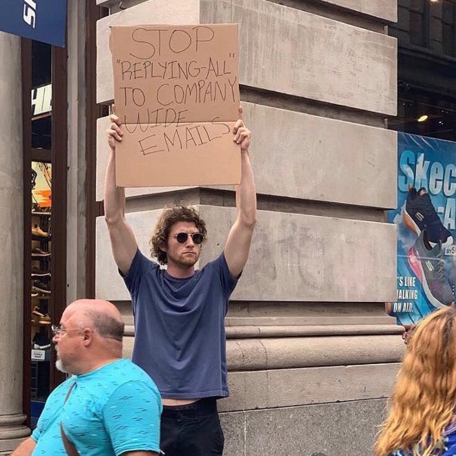 This meme is a photo of a person holding a sign that reads "Stop 'replying all' to company-wide emails". The image is likely meant to be humorous, as it implies that someone is intentionally sending emails to the entire company when a more private response would be sufficient. The sign is being held up in a public place, likely at a protest or demonstration, to raise awareness about this issue.